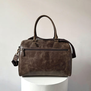 Brown leather duffel bag on a white pedestal against a light gray background