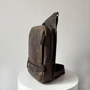 Brown leather sling bag on a white pedestal against a light gray background