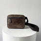 Brown leather crossbody bag on a white pedestal with a light gray background