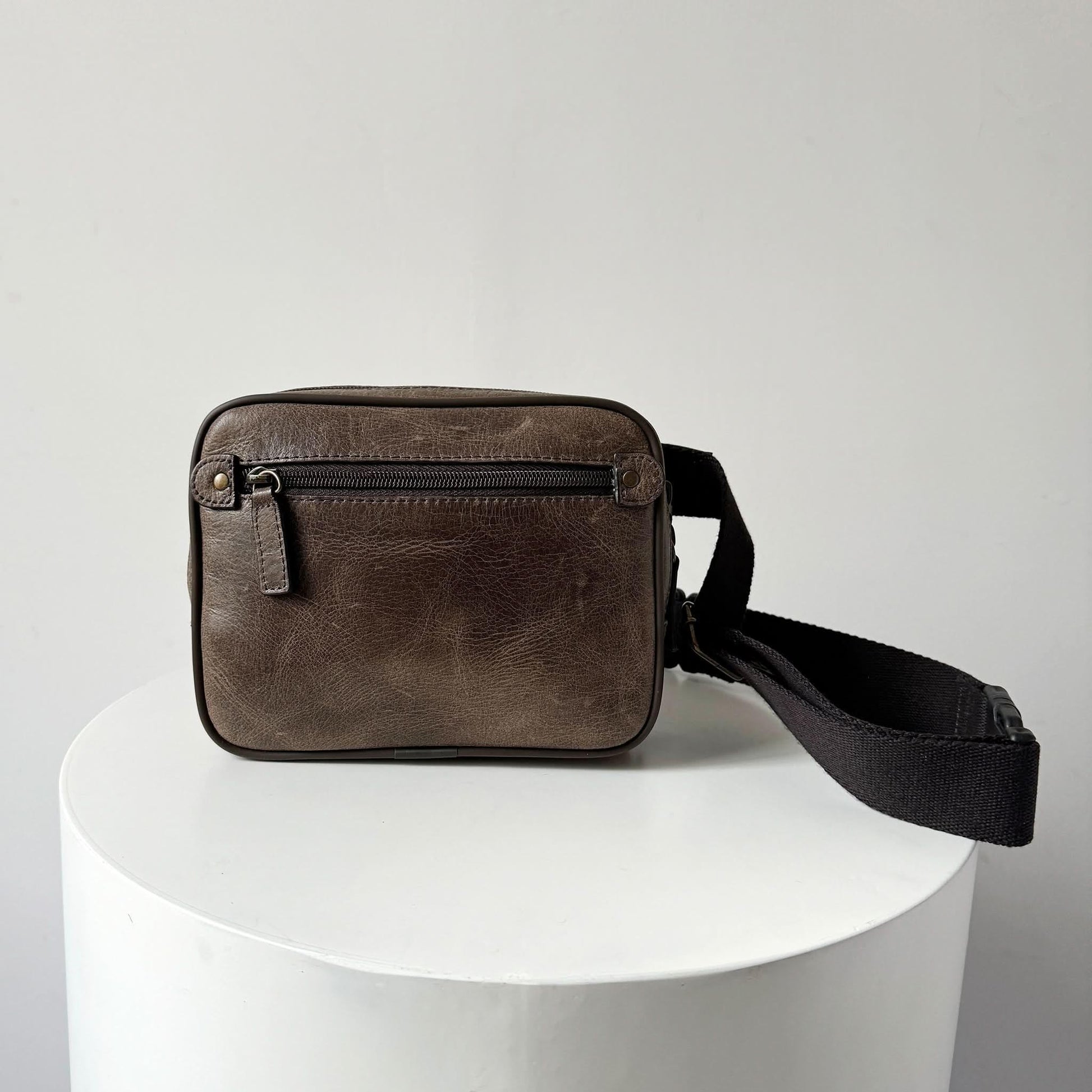 Brown leather crossbody bag on a white pedestal with a light gray background