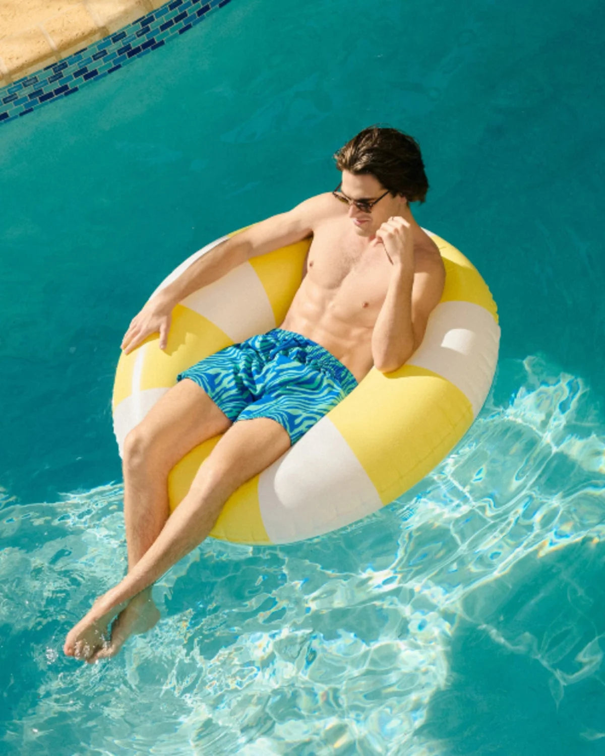 Man relaxing on a yellow and white inflatable ring in a pool