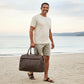 Man holding a brown leather bag on a beach with ocean and sky in the background