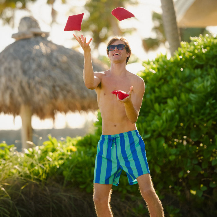 Man in Coastal Cabana Ocean and Palm hybrid swim shorts, a blue and green cabana stripe