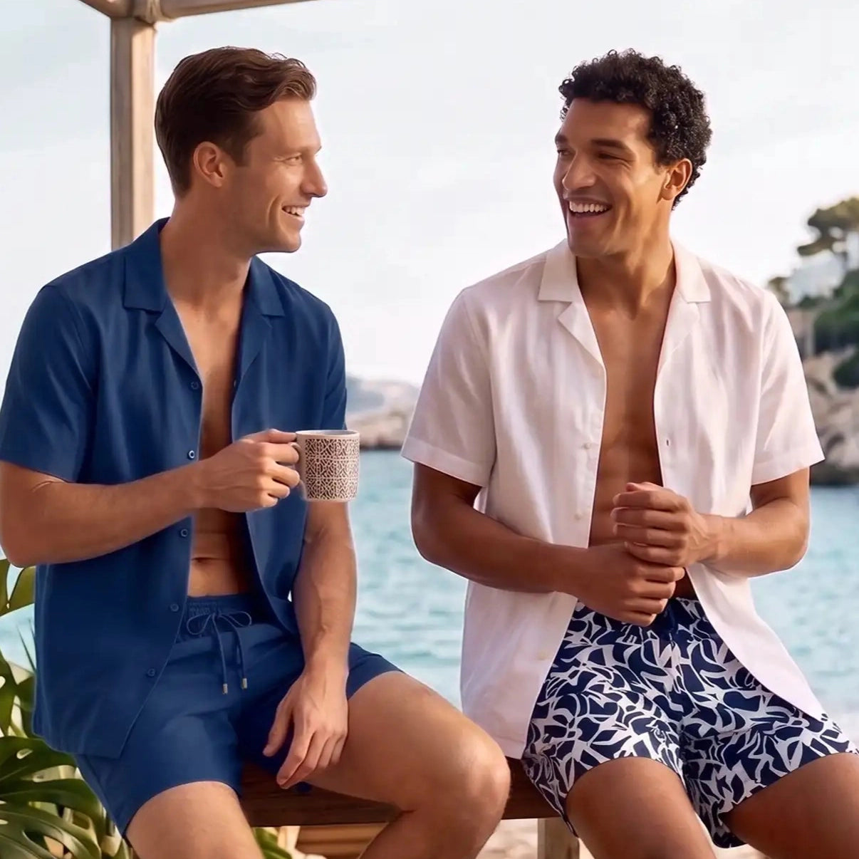 Two men under a cabana, one in a Blue Sapphire resort shirt and matching shorts, one in a white shirt with printed hybrid swim shorts