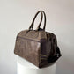 Brown leather duffel bag on a white pedestal against a light gray background
