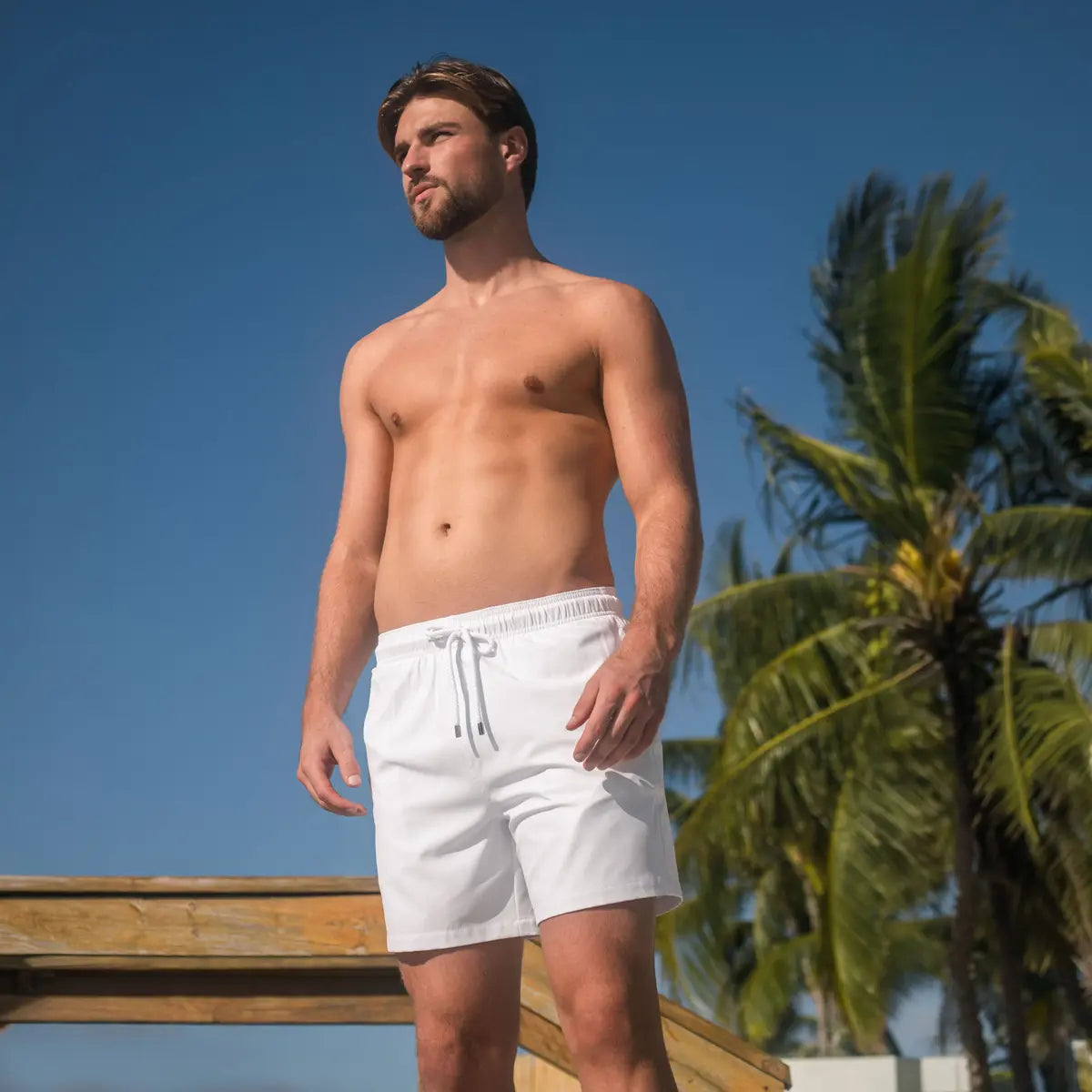 Man in Arctic White hybrid swim shorts in solid white, outdoors by the water