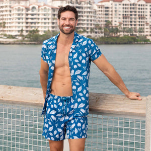 Man beside a waterfront pool in an Autumn Blue resort shirt and matching teal leaf print hybrid swim shorts