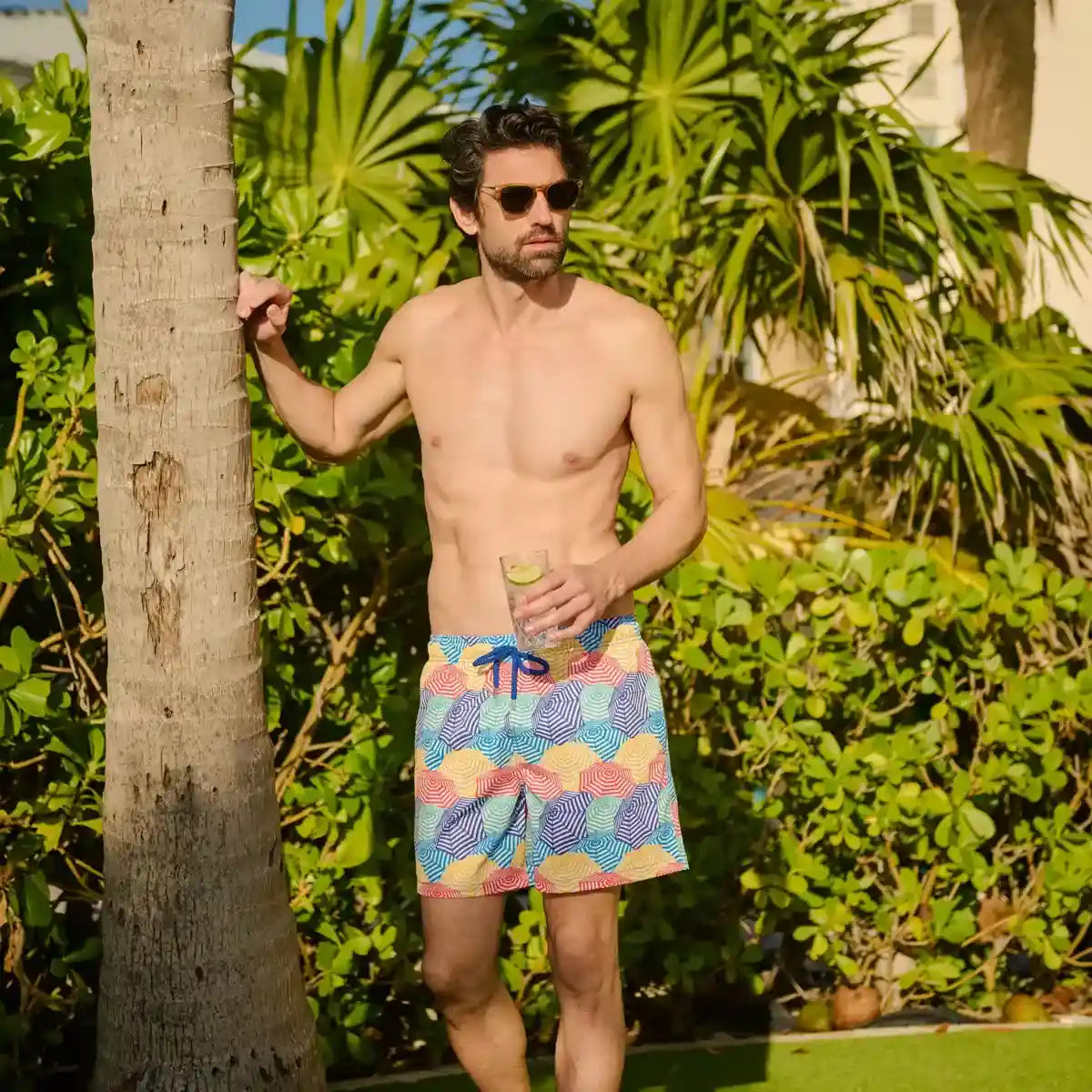 Man in Bayside Shade Splash hybrid swim shorts, multicolor beach umbrella print, at the water