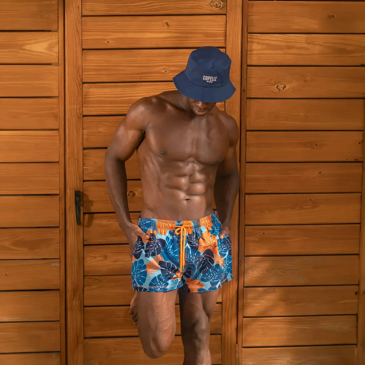 Man in Blue Jungle hybrid swim shorts in the 3 inch Short, blue and orange tropical leaf print, outdoors