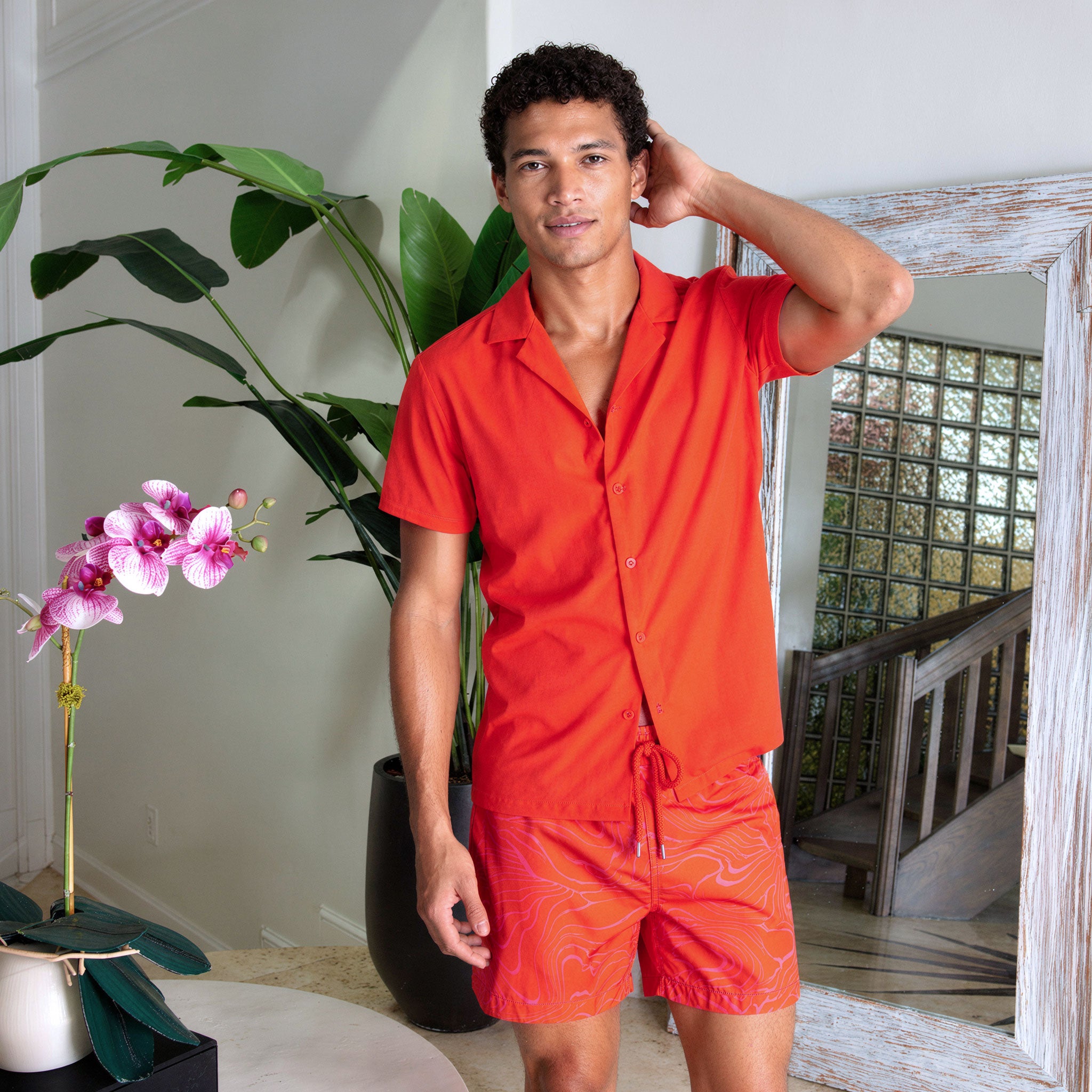 Man in a Coral resort shirt worn open over Sand Waves Heat and Bloom hybrid swim shorts