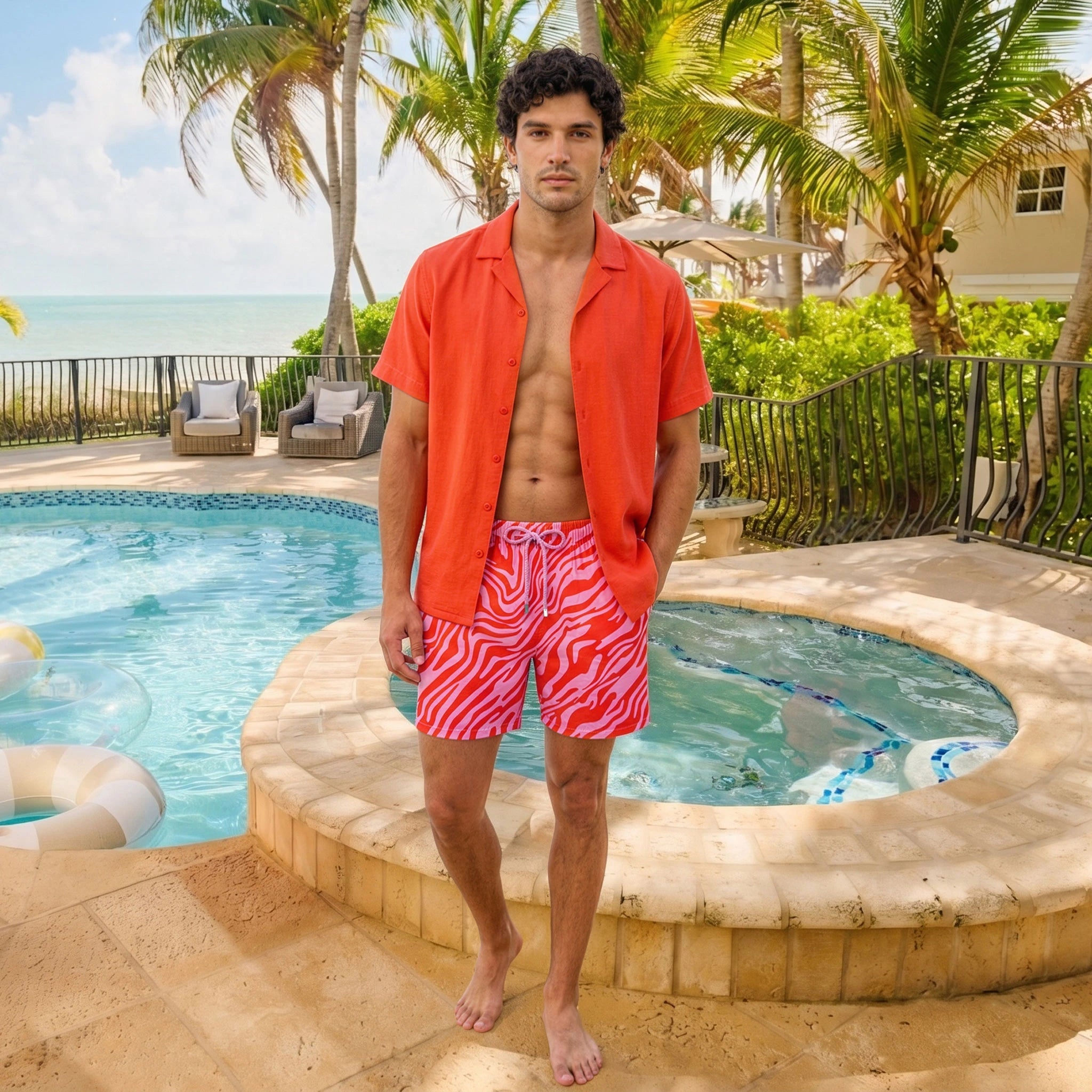Man beside a pool in a Coral resort shirt worn open over coral and pink printed hybrid swim shorts