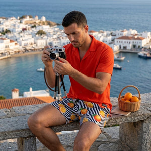 Man with a camera above a harbour in a Coral resort shirt and printed hybrid swim shorts