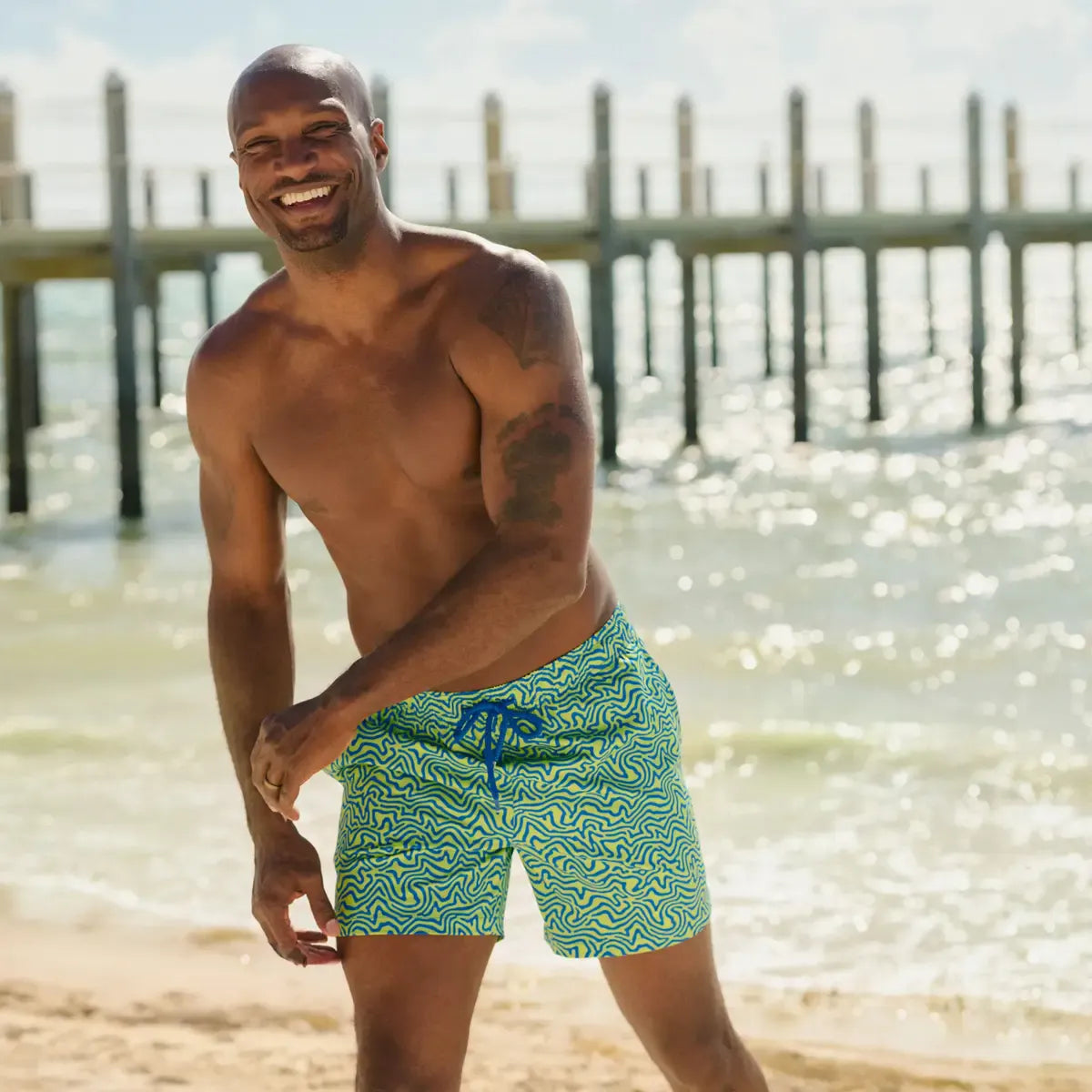 Man in Deco Maze Key Lime hybrid swim shorts, lime and blue swirled maze print, outdoors