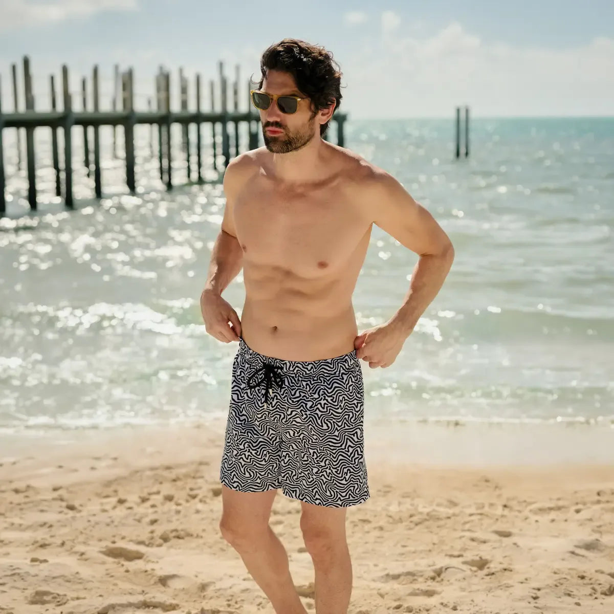 Man in Deco Maze Surf and Storm hybrid swim shorts, black and white swirled maze print, at the water