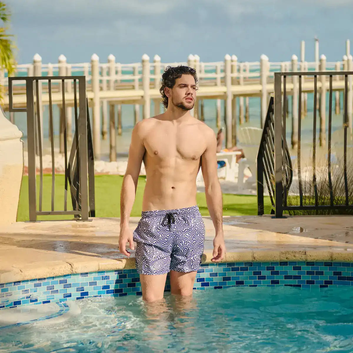 Man in Deco Maze Surf and Storm hybrid swim shorts, black and white swirled maze print, outdoors at a resort