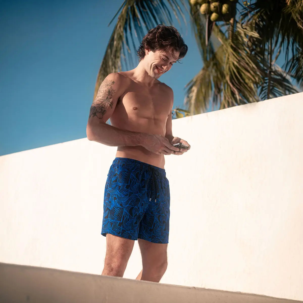 Man in Enigma hybrid swim shorts, royal blue with a navy leaf outline print