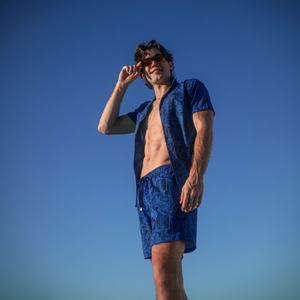 Man against a clear blue sky in an Enigma resort shirt and matching royal blue leaf print hybrid swim shorts