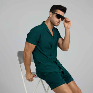Man in a Night Green resort shirt and matching deep green hybrid swim shorts, wearing sunglasses, studio view
