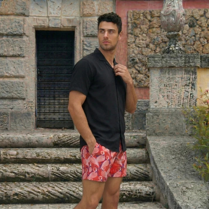 Man on stone steps in a Black Onyx resort shirt and Pink Flamingo hybrid swim shorts