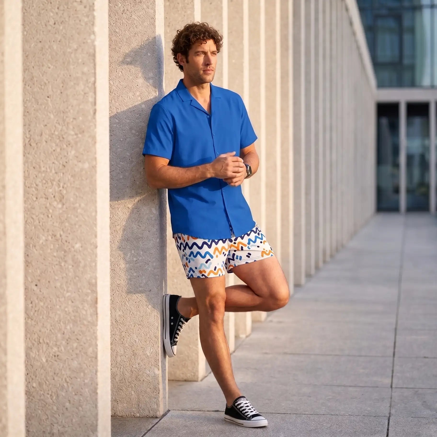 Man in a Line Rush Ocean and Sol hybrid swim short and blue resort shirt, leaning against a concrete wall in the city