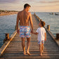 Man and child walking hand-in-hand on a wooden pier by the sea at sunset.
