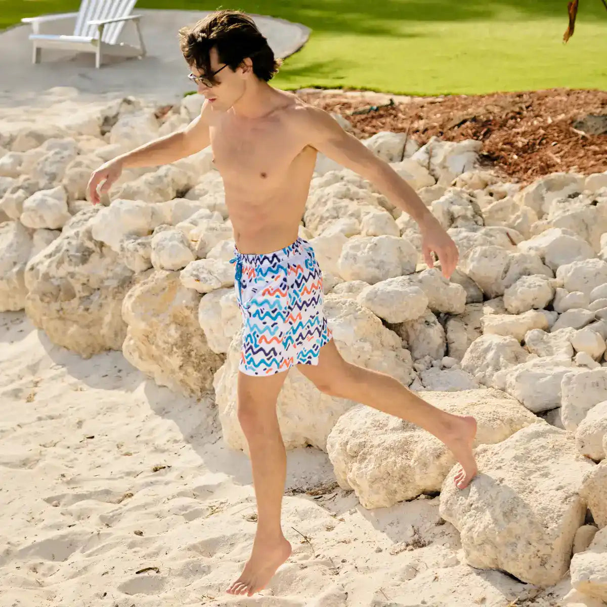 Man in Line Rush Ocean and Sol hybrid swim shorts, navy, aqua and coral zigzag print, outdoors at a resort