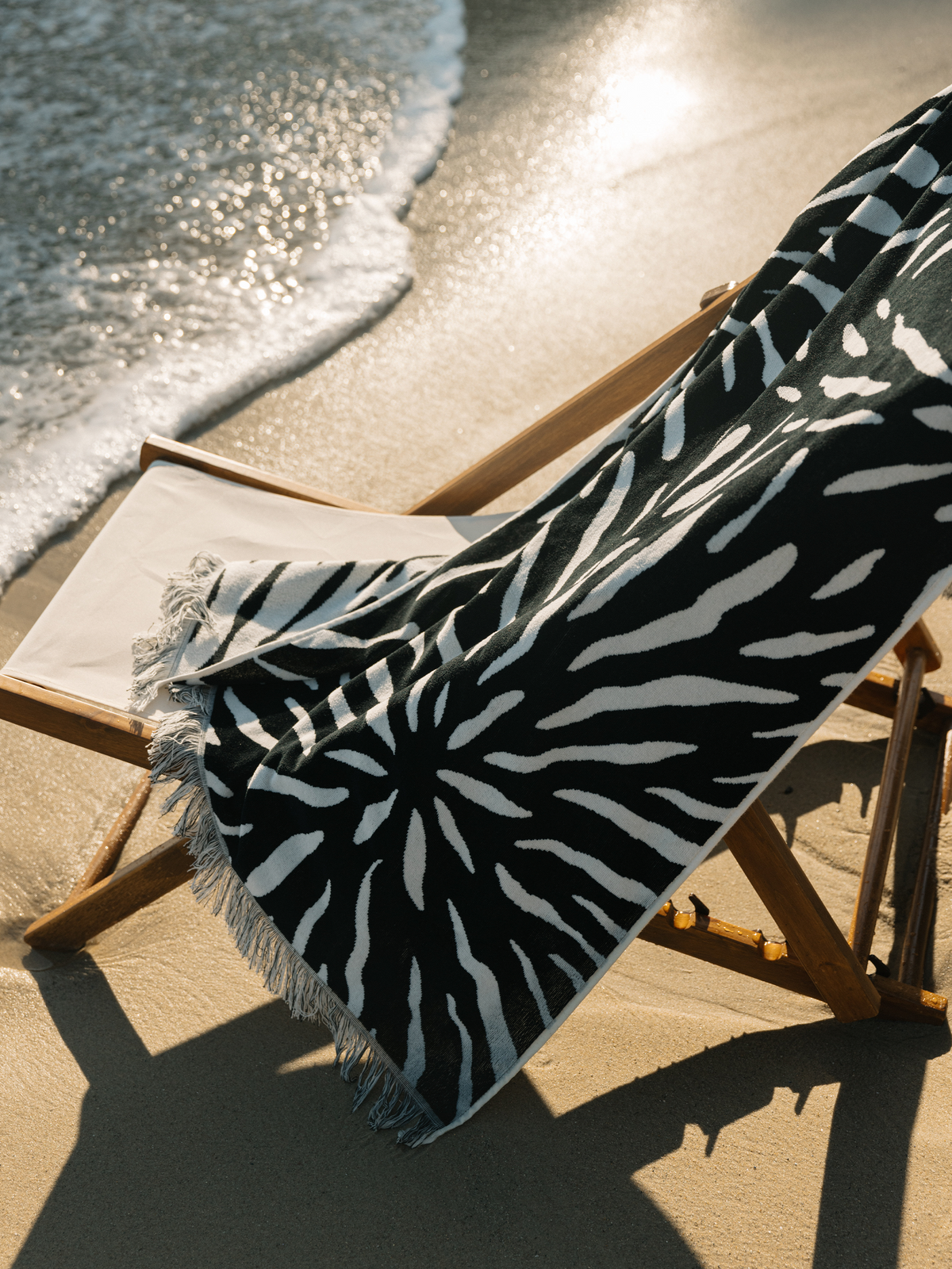 Ruby Mint Remington black and white floral stripe towel on a beach chair by the ocean