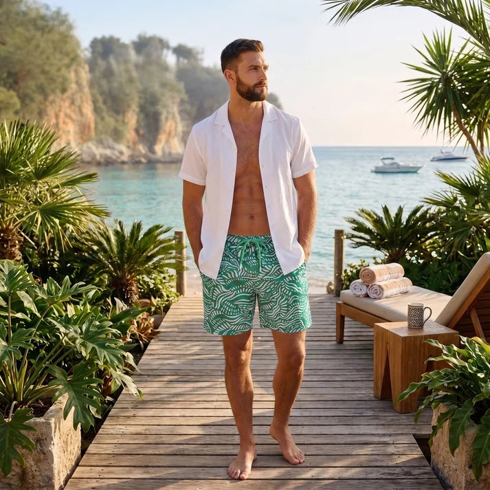 Man on a coastal boardwalk in an Arctic White resort shirt worn open over Salt Spray Palm and Surf hybrid swim shorts