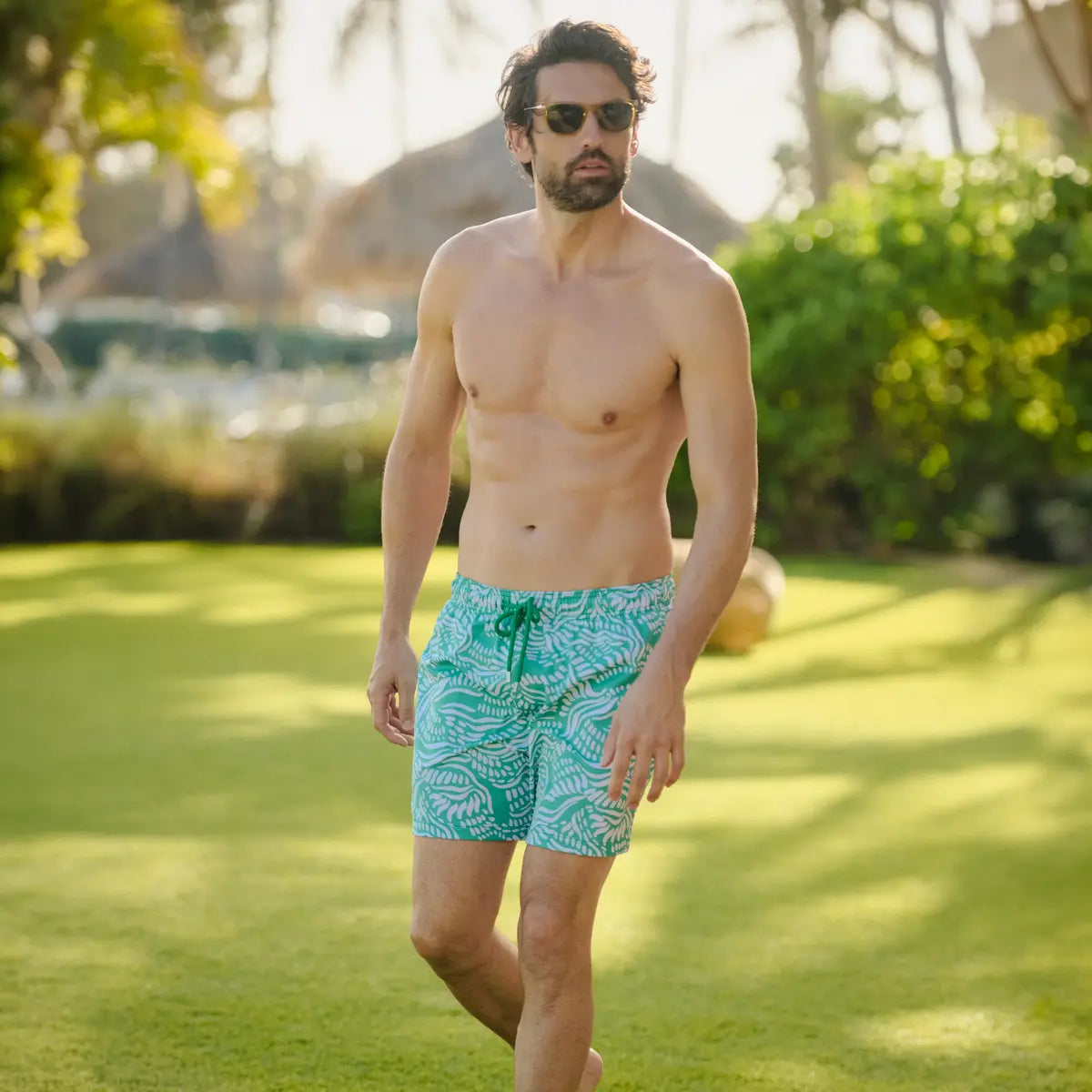 Man in Salt Spray Palm and Surf hybrid swim shorts, jade green with a white coral reef print