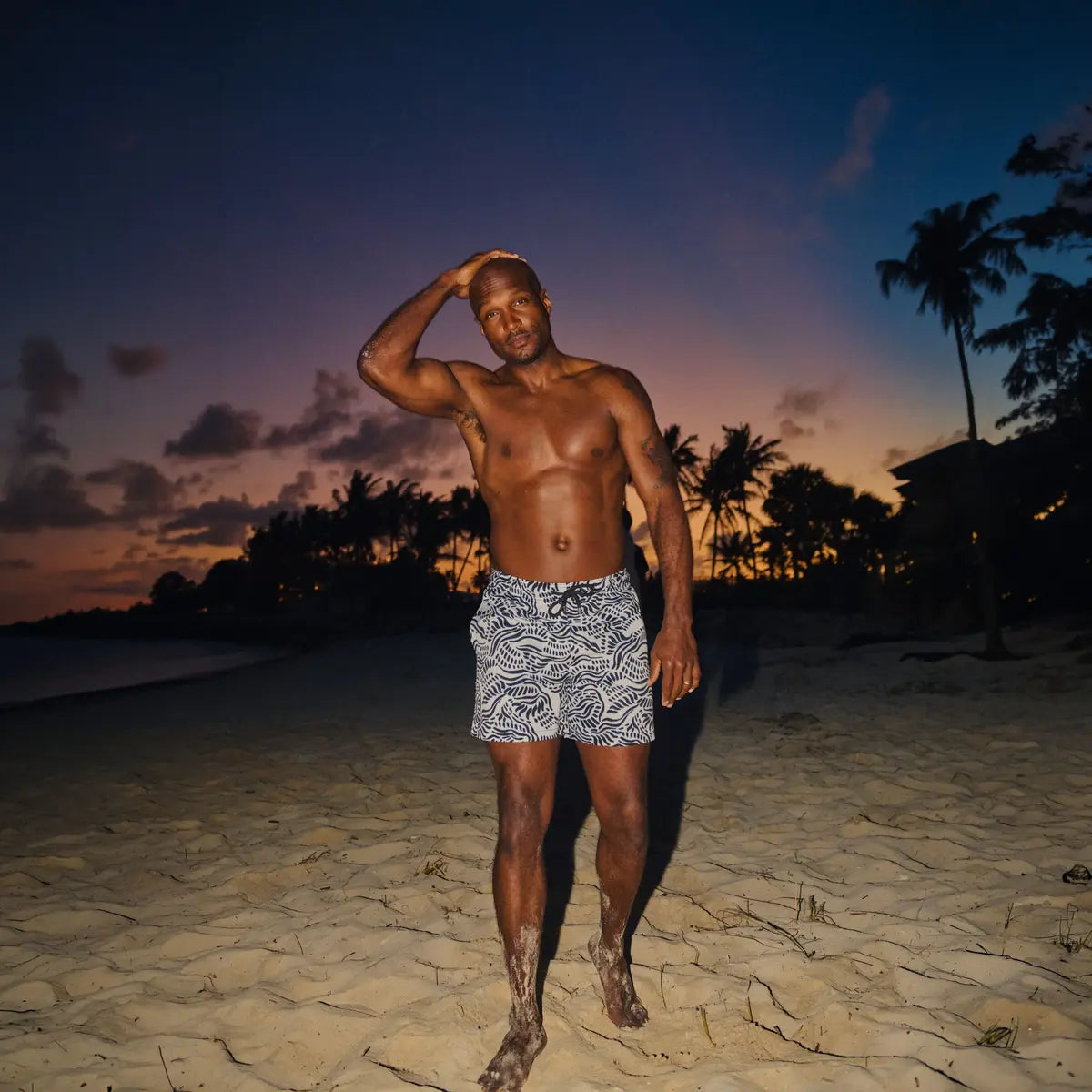 Man in Salt Spray Surf and Storm hybrid swim shorts, black with a white coral reef print, at the water