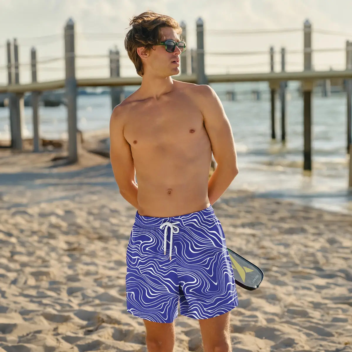 Man in Sand Waves Harbor and Surf hybrid swim shorts, cobalt with a white wave line print, at the beach