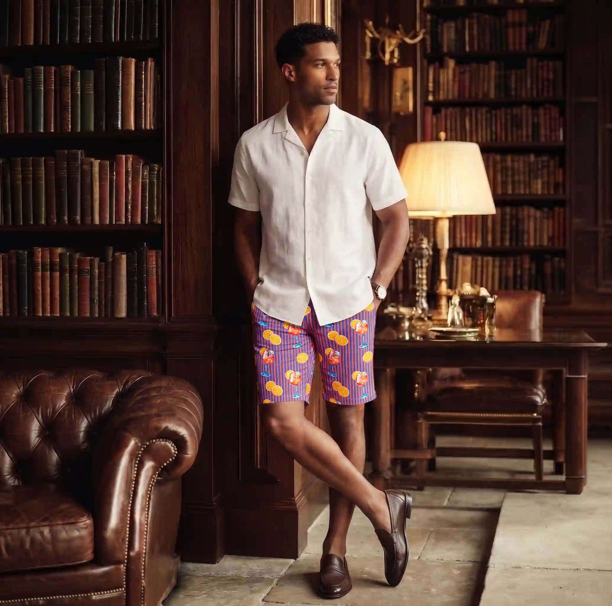 Man in a wood panelled library in Sunset Spritz Ocean and Heat hybrid swim shorts and a white linen resort shirt
