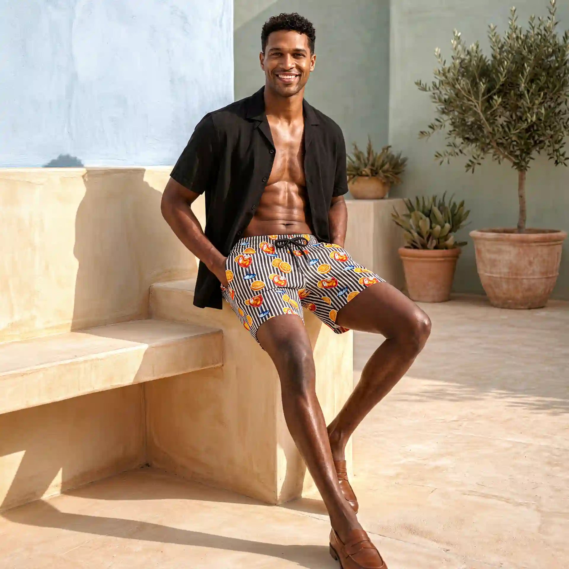 Man seated on a stone bench in Sunset Spritz Surf and Storm hybrid swim shorts and an open black resort shirt