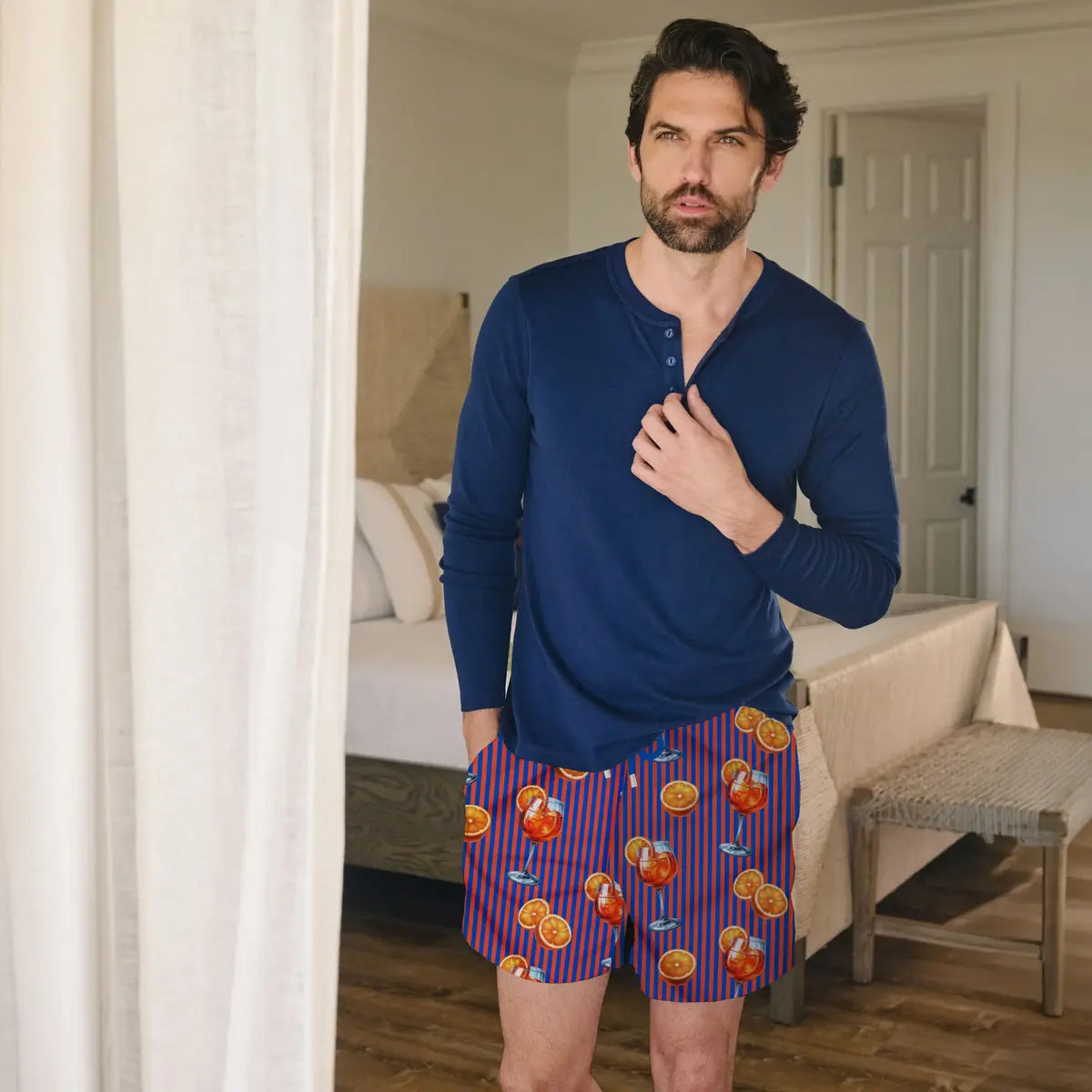 Man in Sunset Spritz Ocean and Heat hybrid swim shorts, a purple and coral stripe with a spritz cocktail print
