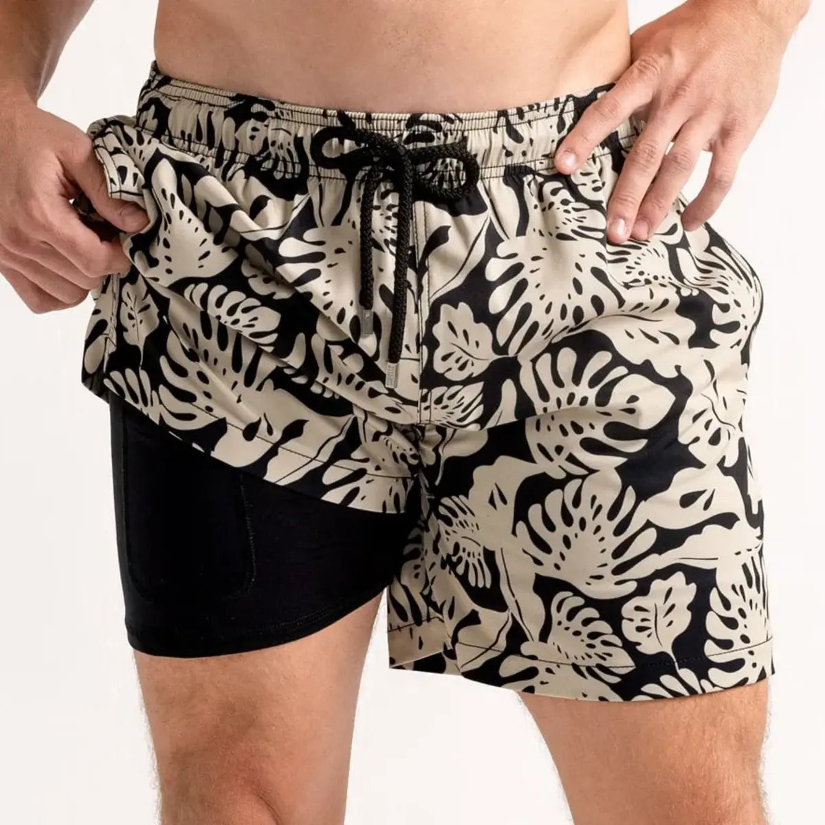 Tropical Garden men's hybrid swim short, black with a cream monstera leaf print, front view showing the black compression liner