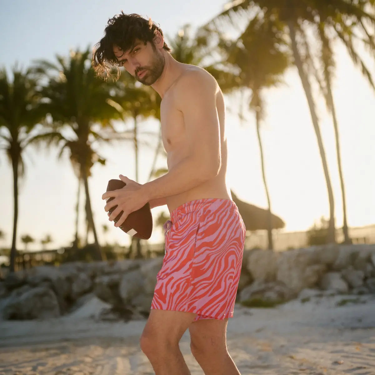 Man in Tropical Swirl Coral and Orchid hybrid swim shorts, a coral and pink swirled print