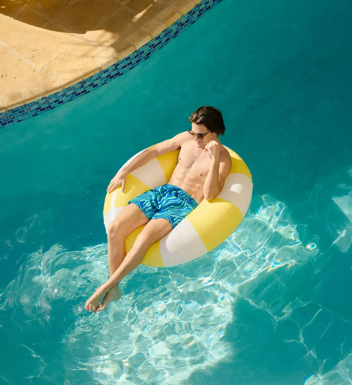 Man in Tropical Swirl Ocean and Palm hybrid swim shorts, blue and green swirled print, at the water